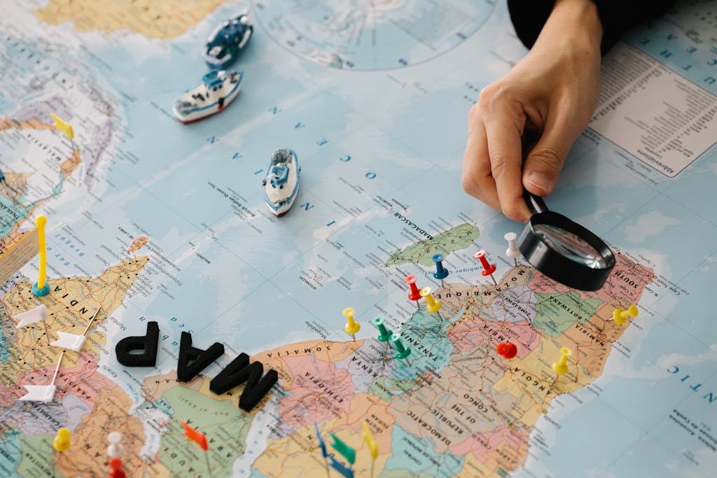 juntos seguros map A hand using a magnifying glass over a world map with pins and toy ships.