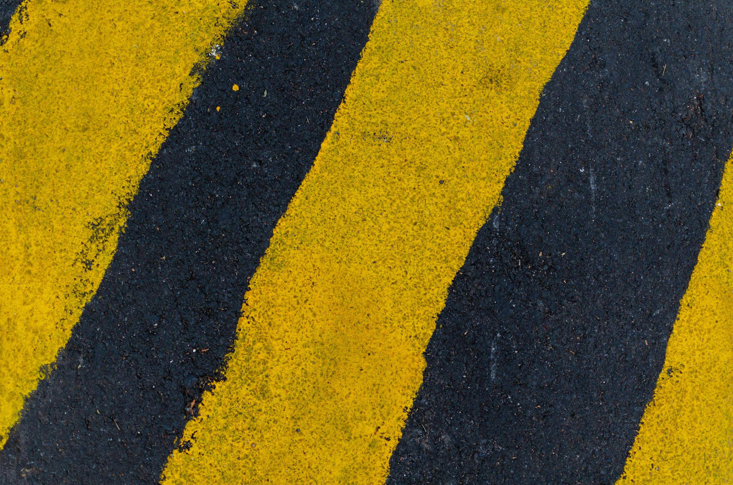 Mansutfer A high-angle close-up of yellow and black road markings on asphalt surface.