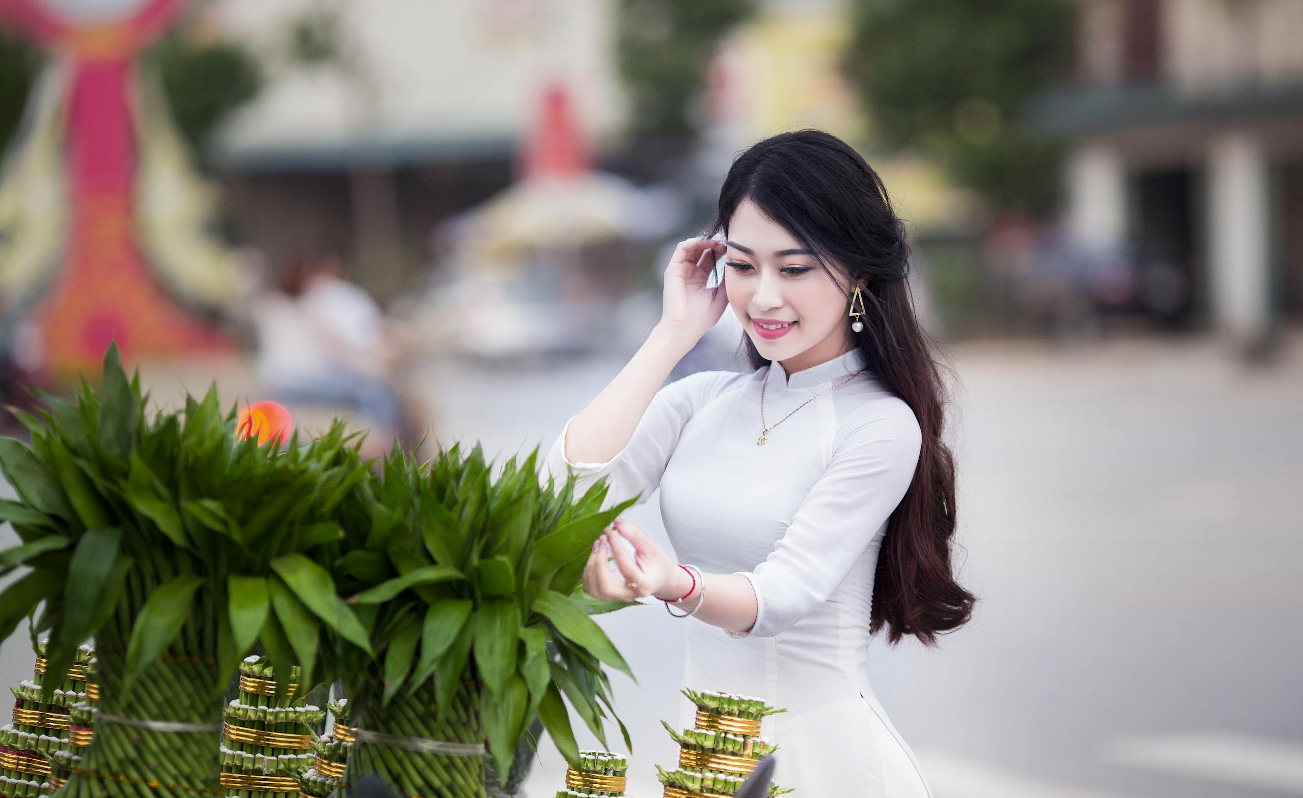 FintechAsia A smiling woman in a white dress near lush greenery outdoors, exuding joy.