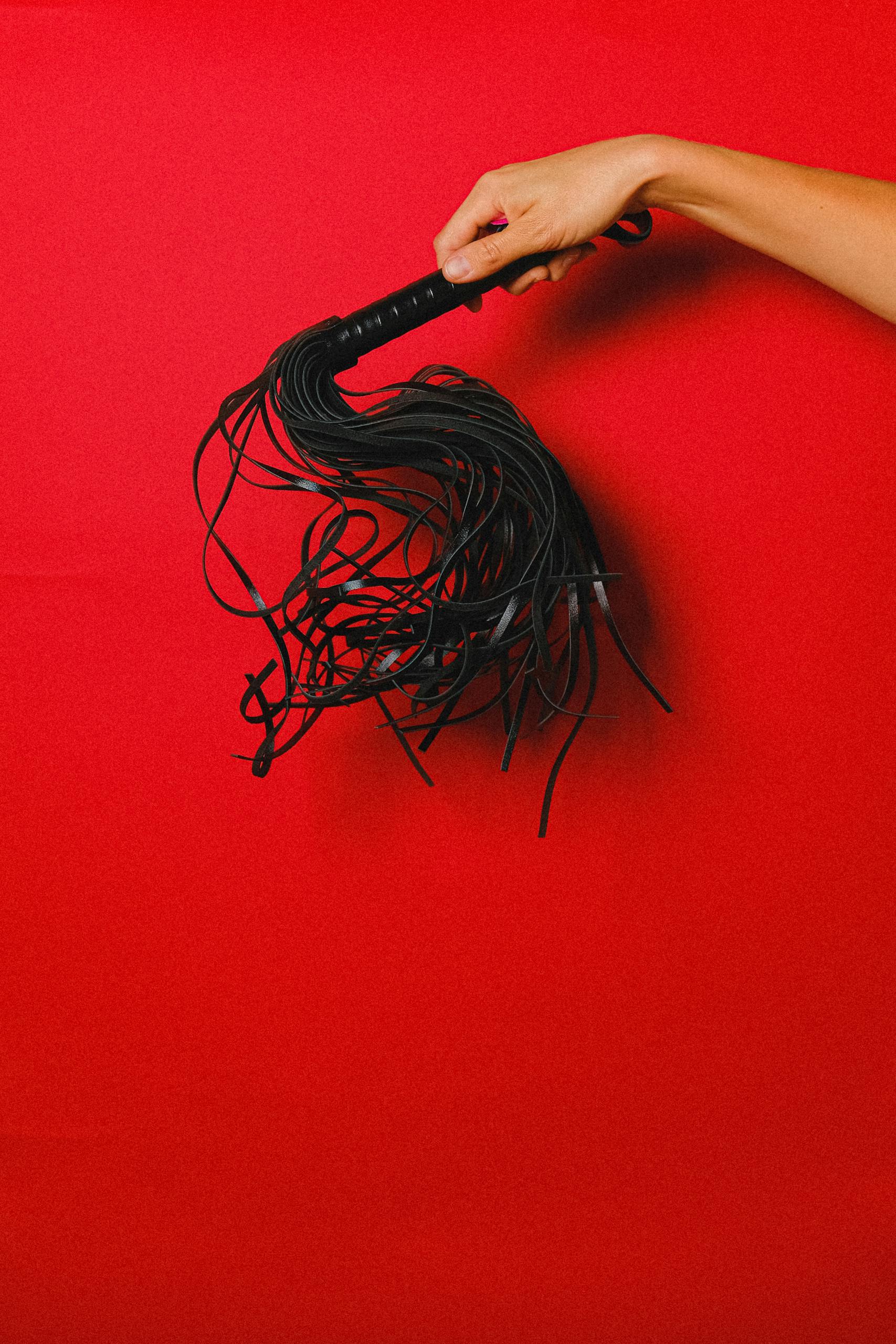 TRIOS 5 Invisalign Submission Black leather whip held by a hand on a vibrant red backdrop, symbolizing passion and sensuality.