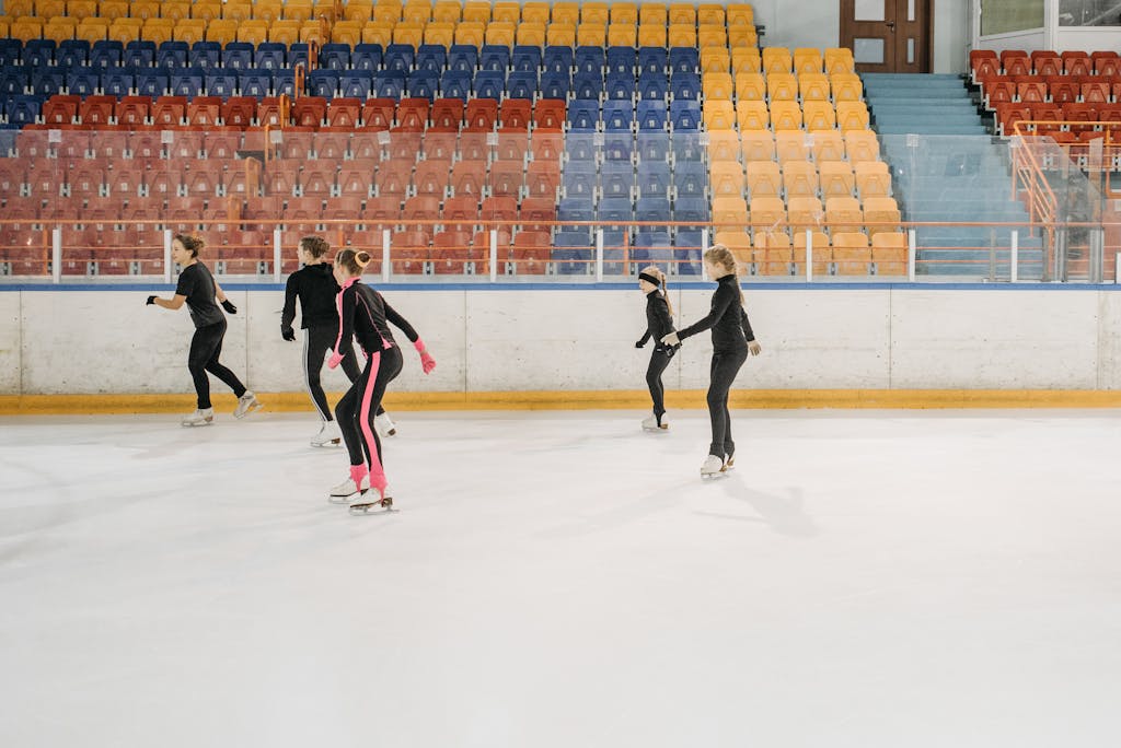 Juntos Seguros I Five young skaters practice figure skating on an indoor ice rink, focusing on teamwork and technique.