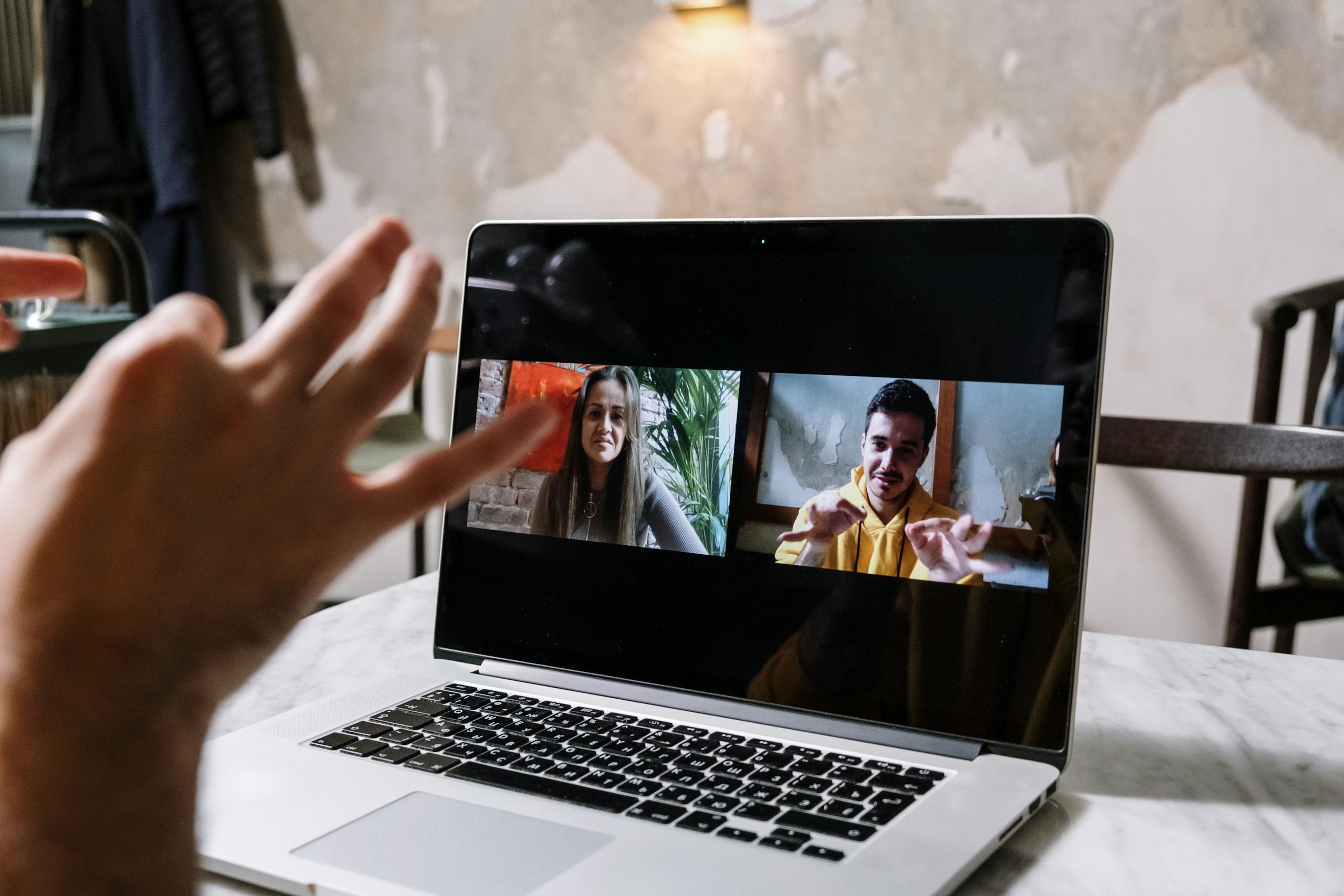 SocialMediaGirls Forum Hands gesturing during a video call on a laptop screen, showing two people in a virtual meeting.