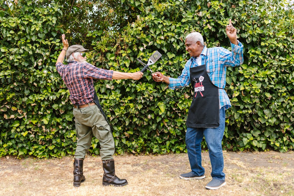 Weber Grillvorführung Two senior men having fun with barbecue tools in a garden setting.