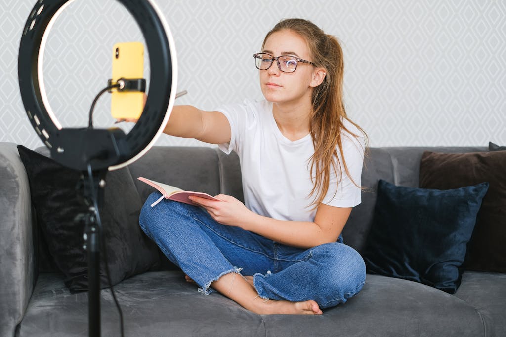 Beriful Woman vlogging with smartphone and ring light while holding a book on a sofa.