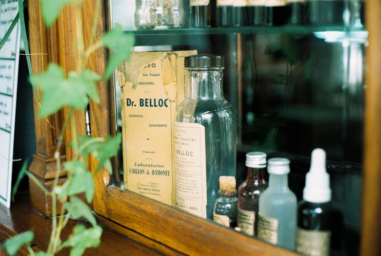 Memorandum to Cabinet A collection of vintage apothecary glass bottles in a wooden cabinet.