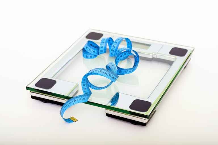 digitalconnectmag.com A digital glass weighing scale with a blue measuring tape, symbolizing weight management.
