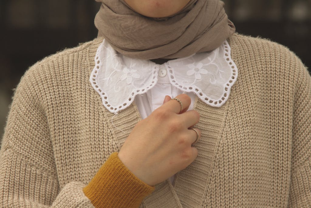 Carmela Clouth Close-up of a woman wearing a beige cardigan with a lace collar and rings.